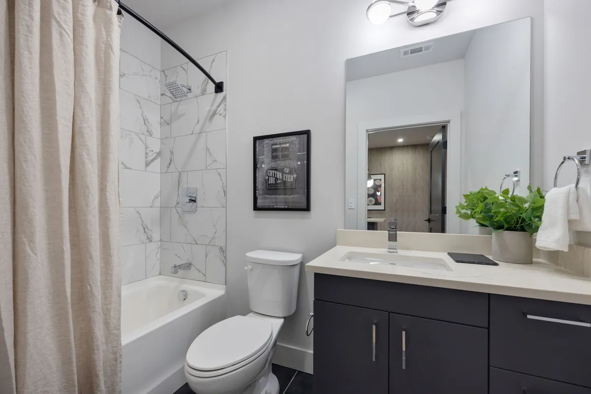 A serene bathroom with a bathtub, vanity with a sink, framed artwork, and a potted plant. The scene exudes calm, inviting guests to indulge in refreshing morning routines or tranquil evening baths.