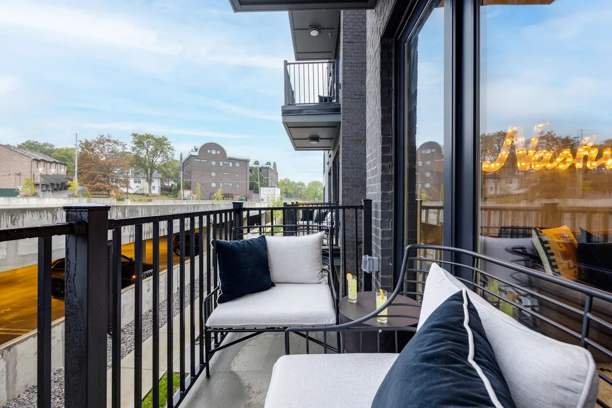 A private balcony with comfortable seating overlooking the city skyline, highlighted by a neon sign and inviting atmosphere. The view captures both the vibrancy of the city and a sense of relaxed privacy, perfect for morning coffee or evening cocktails.