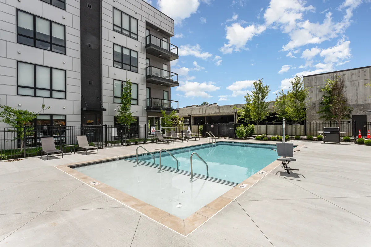 A vibrant exterior shot featuring a sparkling swimming pool surrounded by lounge chairs and balconies, with lush landscaping creating a resort-like atmosphere. The pool area invites relaxation and social gatherings, evoking a sense of leisure and fun.