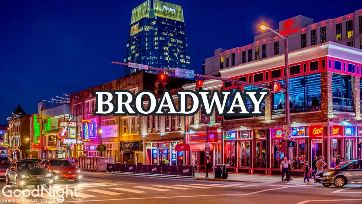 A vibrant city street scene at night with neon signs, busy sidewalks, and a variety of restaurants and bars. The street is alive with people walking and engaging in nightlife activities, capturing the energetic pulse of Nashville after dark.