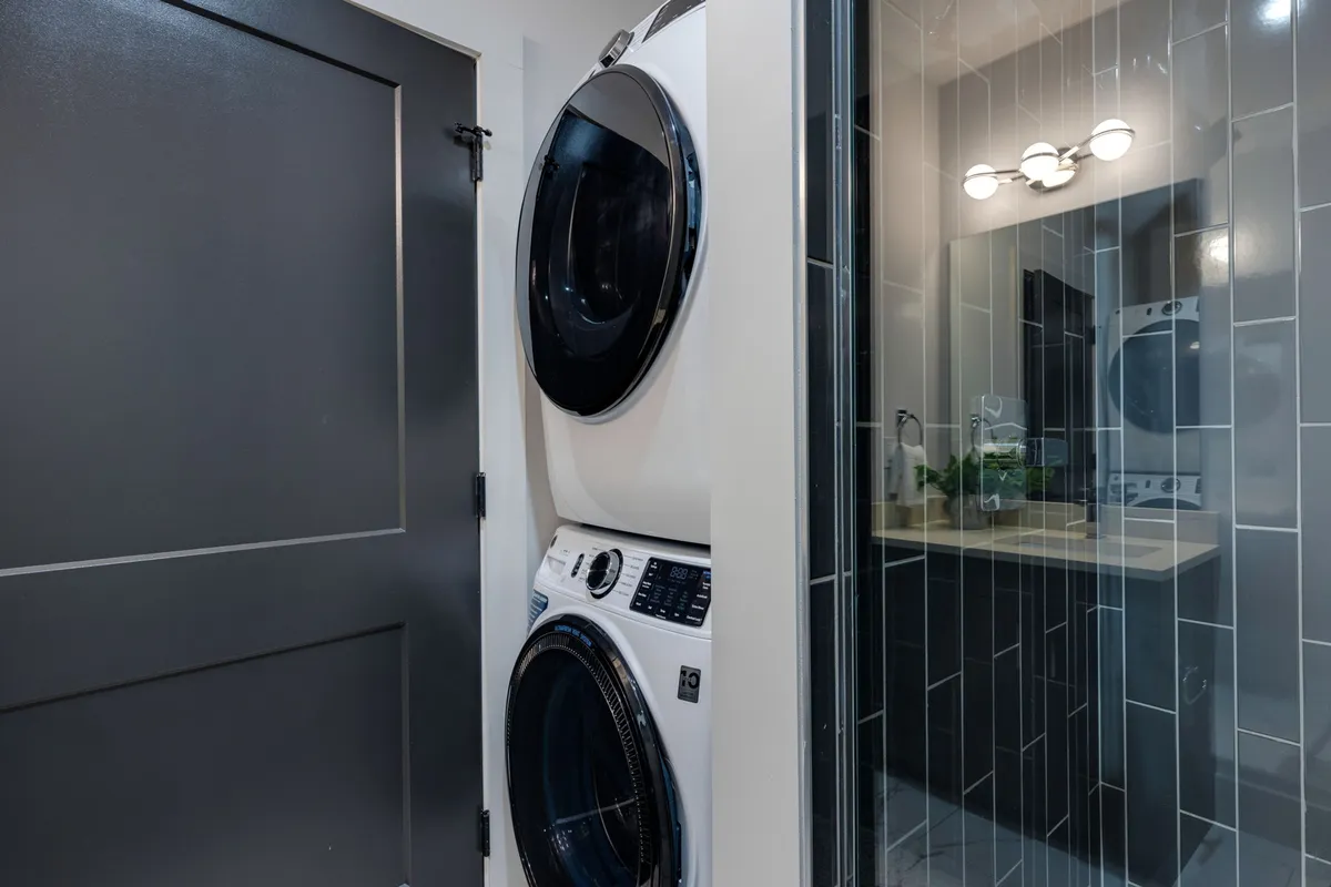 This image highlights a stacked washer and dryer situated in a well-organized laundry space, with a mirror and sink also visible. The setup looks efficient, clean, and user-friendly, emphasizing the convenience of in-unit laundry for families and business travelers alike.